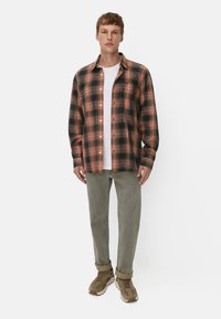 Rutet skjorte med knapper i orange, sort og grøn; kombineret med en hvid T-shirt og olivengrønne bukser; afsluttet med beige sneakers.