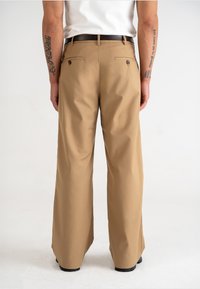 Khaki wijde broek met een gladde textuur, twee achterzakken en een bruine riem. Eenvoudig ontwerp, aansluitend op de taille, valt tot aan de enkels.