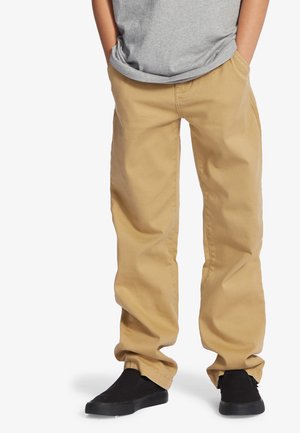 Pantalones cargo caqui hechos de una resistente tela de algodón, con un corte relajado, bolsillos laterales y una textura suave. Llevados con zapatos negros sin cordones.