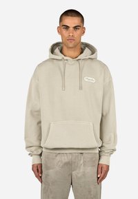 Felpa color crema in morbido cotone misto. Presenta una tasca frontale, cordini regolabili e un piccolo patch logo blu sul petto.