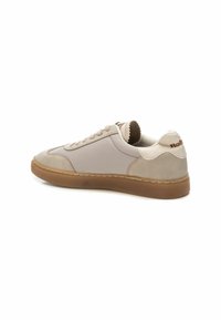 Zapatilla de color beige claro, hecha de cuero y ante. Presenta una suela de goma con un acabado texturizado y acentos cosidos. Logotipo en el talón.