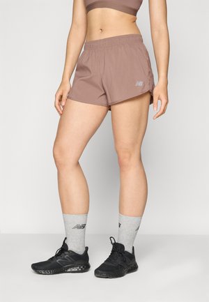Pantaloni scurți sportivi maro cu un braț elastic, având un logo reflexiv. Asortați cu pantofi de alergare negri și șosete gri până la gleznă.