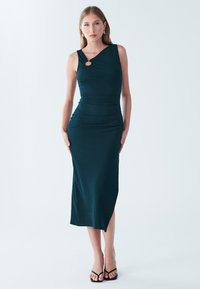 Dark teal ribbed midi dress with a one-shoulder design, featuring a circular accent at the neckline and a side slit. Smooth texture.