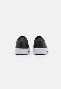 Sneakers neri in pelle con design a profilo basso. Suola in gomma bianca e dettagli di cucitura visibili sul tallone. Texture liscia.