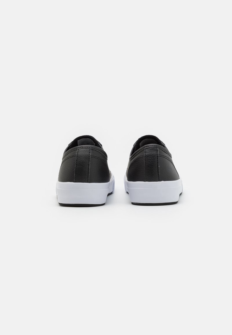 Zapatillas de cuero negro con un diseño de perfil bajo. Suela de goma blanca y detalle de costura visible en el talón. Textura suave.