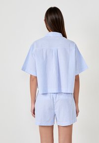 Camicia a maniche corte a righe blu e bianche con colletto abbinata a pantaloni corti coordinati, caratterizzata da una vestibilità comoda e una texture di tessuto liscia.