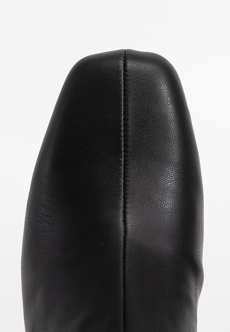 Zapato de cuero negro con punta afilada y textura suave. Cuenta con una costura vertical en la parte frontal para añadir detalle.