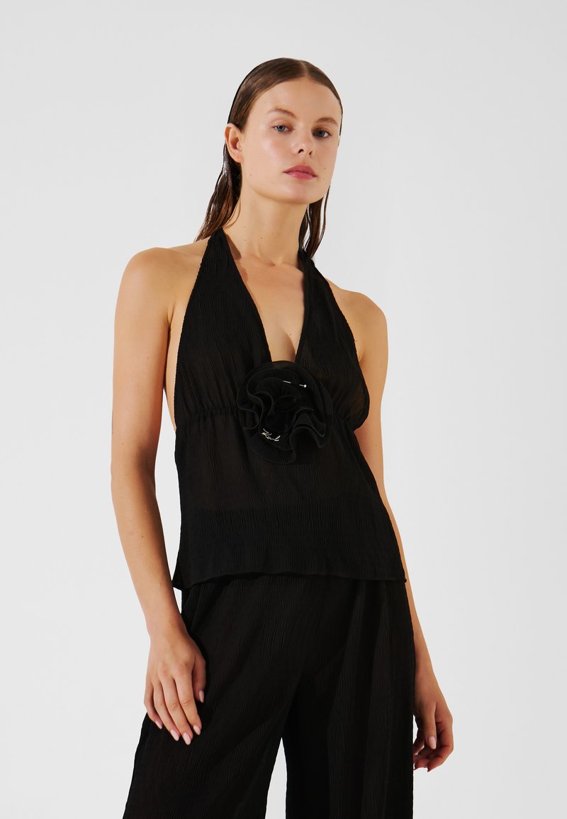 Juodas halterio tipo viršus su klostėmis ir gėlėmis dekoruotu akcentu centre. Lengvas ir plasnumas, pasižymintis laisvu siluetu.