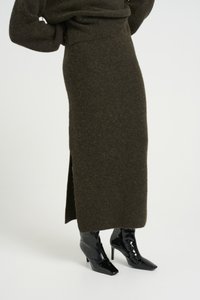 Falda de punto verde oliva con una abertura lateral, combinada con botas negras brillantes de tobillo con puntera afilada y tacones de aguja.