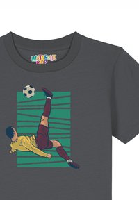 Grijze t-shirt met een afbeelding van een speler in een geel shirt die een trap uitvoert, met een voetbal en een groen gestreepte achtergrond.