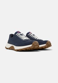 Sneakers in suede blu navy con lacci bianchi, suola in gomma testurizzata e materiali misti. Presentano un'etichetta rossa sulla linguetta.