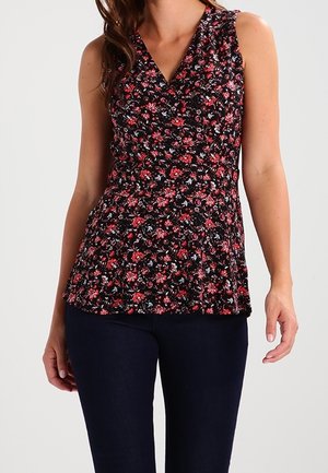 Ærmeløs sort blomsterbluse med v-udskæring, der har små lyserøde og hvide blomster, samleliv og en svævende nederkant. Kombineret med mørke bukser.