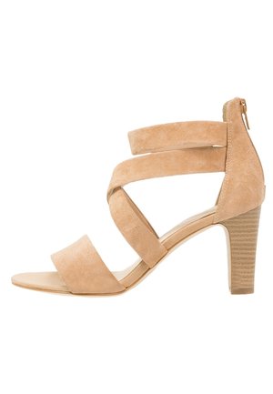 Beige suède sandaal met hak, voorzien van drie brede banden en een rits aan de achterkant. Textuur op de hak met verticale groeven voor grip.