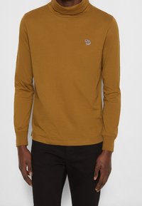 Senfgelbes Langarm-Turtleneck-Shirt aus weichem Stoff mit einer kleinen mehrfarbigen Tierstickerei auf der linken Brust.