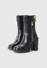 Zwarte leren enkelboots met een chunky hak, zijrits en een gouden hartaccent op de band. Glad textuur en slank ontwerp.