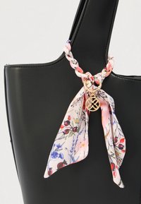 Μαύρη τσάντα ώμου από δέρμα με πλεκτό μαντήλι με λουλούδια δεμένο στη λαβή, με χρυσό κυκλικό μενταγιόν με σχέδιο κοπής.