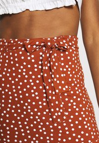 Falda marrón con lunares hecha de un tejido suave, que presenta una cinturilla anudada y patrones circulares blancos en todo el material.