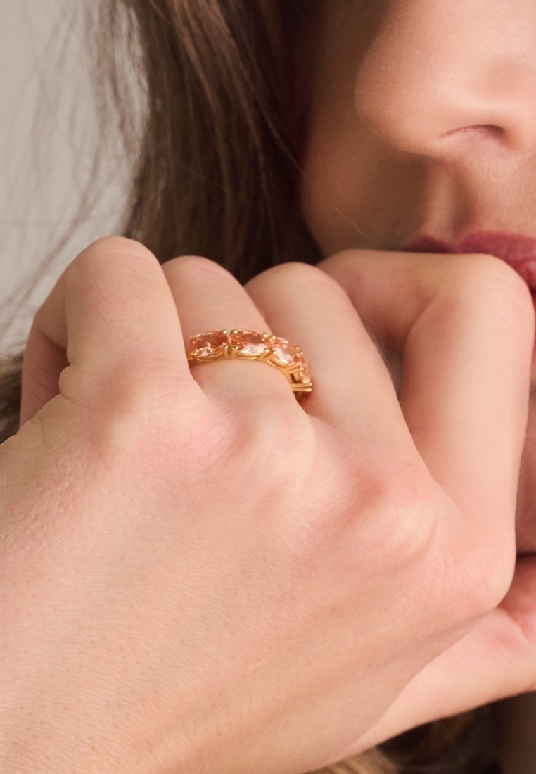 Goldring mit mehreren pinken Steinen in einem einzigartigen Design, auf einer Hand mit heller Hautfarbe präsentiert. Glatte Textur mit glänzender Oberfläche.
