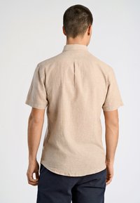 Kortärmad skjorta i ljusbeige linne, med spetskrage, ryggveck och rundad nederkant. Enkel, strukturerad tyg.