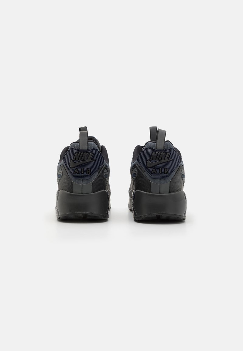 Baskets Nike Air en marine foncé et noir, présentant une tige texturée, des languettes de traction et un branding visible sur le talon et les côtés.