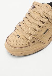 Light brown sneaker with perforated detailing, thick laces, and rubber sole. Features brand logo near the ankle and textured sides.