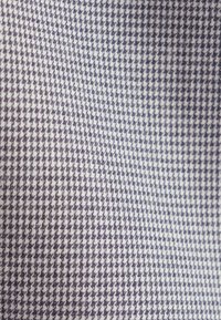 Tissu présentant un motif pied-de-poule en marine et blanc, affichant une texture tissée avec de petites formes alternées tout au long.