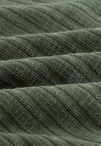 Close-up van gevouwen olijfgroen stof met diagonale geribbelde breistructuur en zachte, zichtbare vezels.