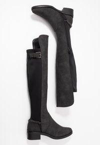Botas negras sobre la rodilla con una suave textura de ante, paneles elásticos, cremallera lateral y acento de cadena cerca del tobillo. Tacón ancho y resistente.