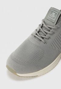 Baskets de sport grises claires en maille respirante, dotées d'un empiècement avant texturé, de lacets plats et d'une étiquette de marque sur la languette.