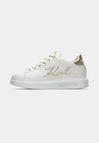 Adidași din piele albă cu accente aurii, logo semnătură pe lateral, vârf rotund și talpă groasă, texturată.