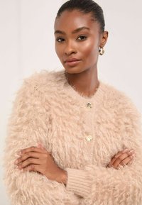 Vattacukor bézs kardigán, textúrált, plüss szálakkal, kerek nyakkivágással és arany gombokkal, bordázott mandzsettákkal és laza fazonban.