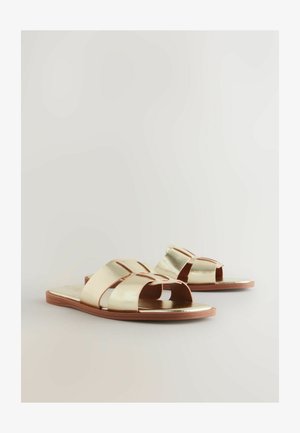 Gouden metallic slidesandalen met brede gekruiste banden, open teen ontwerp en platte bruine zool. Gladde textuur met een minimalistische esthetiek.