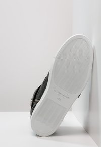 Czarne skórzane buty z białą gumową podeszwą o falistym wzorze bieżnika, rozmiar 40½, markowe Cesare Casadei, opierające się o białą ścianę w rogu.