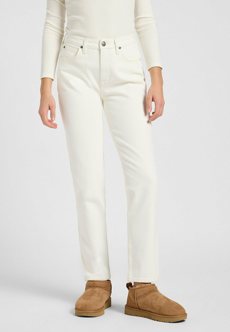Jeans de denim blanco con corte recto, con bolsillos delanteros y cierre de botón estándar, combinados con botines de ante marrón.