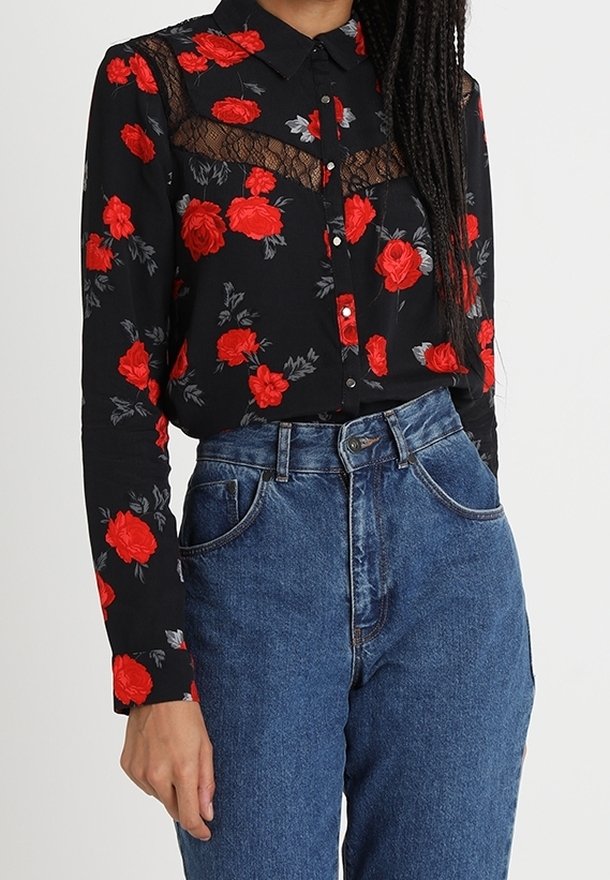 Blusa nera a maniche lunghe con fiori, caratterizzata da rose rosse, pannello in pizzo sul petto, chiusura a bottoni e colletto. Indossata con jeans di denim a vita alta.