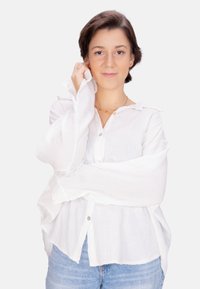 Weißes, strukturiertes Hemd mit langen Ärmeln und leicht übergroßer Passform; getragen mit blauen Jeans. Einfaches, Kragen-Design und neutrale Farbe.