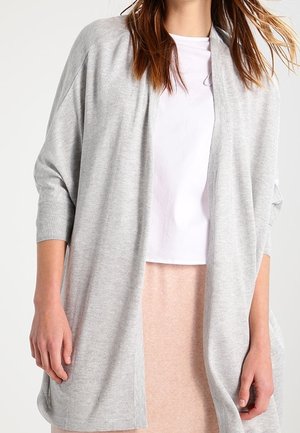 Cardigan grigio chiaro con una vestibilità rilassata, dotato di maniche a tre quarti, design aperto e morbido tessuto a maglia. Indossato sopra un top bianco.
