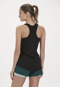 Svart träningslinne med racerback-design, i kombination med grönmönstrade shorts som har en ljusgrön kant.