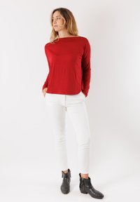 Maglietta rossa a maniche lunghe con una vestibilità rilassata, abbinata a pantaloni bianchi slim-fit e stivali neri alla caviglia con dettagli in zip.