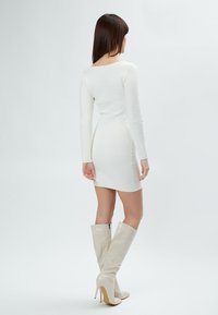 Hvid langærmet kjole med tætsiddende pasform og tekstureret mønster. Kombinationen med knæhøje, lysebeige, blanke hælstøvler.