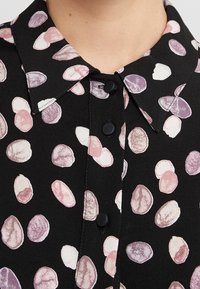 Col de chemise noir avec boutons noirs, présentant des taches ovales abstraites éparpillées dans des nuances de rose, blanc et violet.