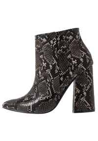 Stivale alla caviglia con tacco alto, in pelle di serpente nera e grigia, con punta appuntita e tacco a blocco su sfondo bianco.