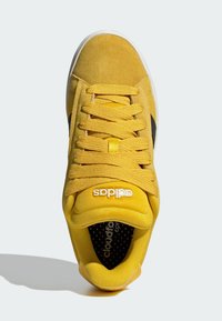 Baskets en daim jaune avec accents noirs, lacets plats et semelle blanche. Comprennent une tige texturée et une semelle intérieure perforée pour la ventilation.