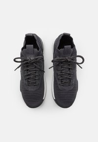 Ett par svarta stickade löparskor med texturerade ovandelar, snören med öglor och vita dämpande sulor mot en vit bakgrund.