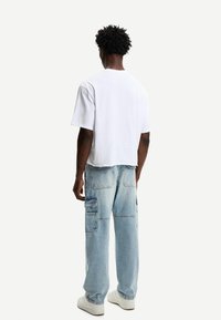 Bijela skraćena majica s kratkim rukavima uparena s svijetloplavim traper hlačama s širokim nogavicama i više džepova. Bijele tenisice.