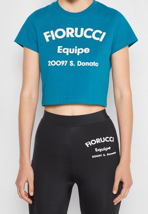Personne portant un t-shirt court bleu et des leggings noirs, tous deux avec le texte blanc « Fiorucci Equipe 20097 S. Donato » imprimé sur le devant.