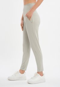 Pantaloni alti grigi chiari realizzati in tessuto elasticizzato, con tasche laterali e design slim-fit, abbinati a sneakers bianche.