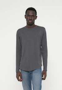 Grijze lange mouwen t-shirt gemaakt van zachte stof, met een ronde halslijn en een iets gebogen zoom, gecombineerd met lichtblauwe jeans.