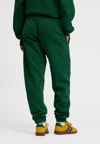 Gröna mjukisbyxor med en avslappnad passform, elastisk midja och muddar. Kombineras med gula och gröna sneakers med en distinkt design.