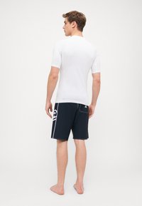 Hvit kortermet rashguard parret med svarte svømmebukser med sideskjold, baklomme og kontrasterende hvite sømdetaljer.